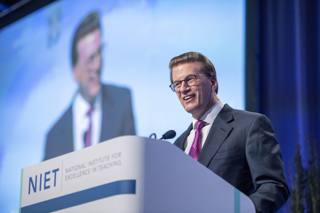 Lowell Milken speaking at a podium 