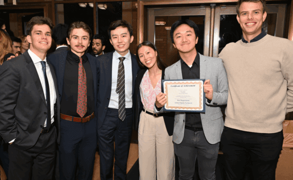 Six students smiling, one of the students is holding a certficate.